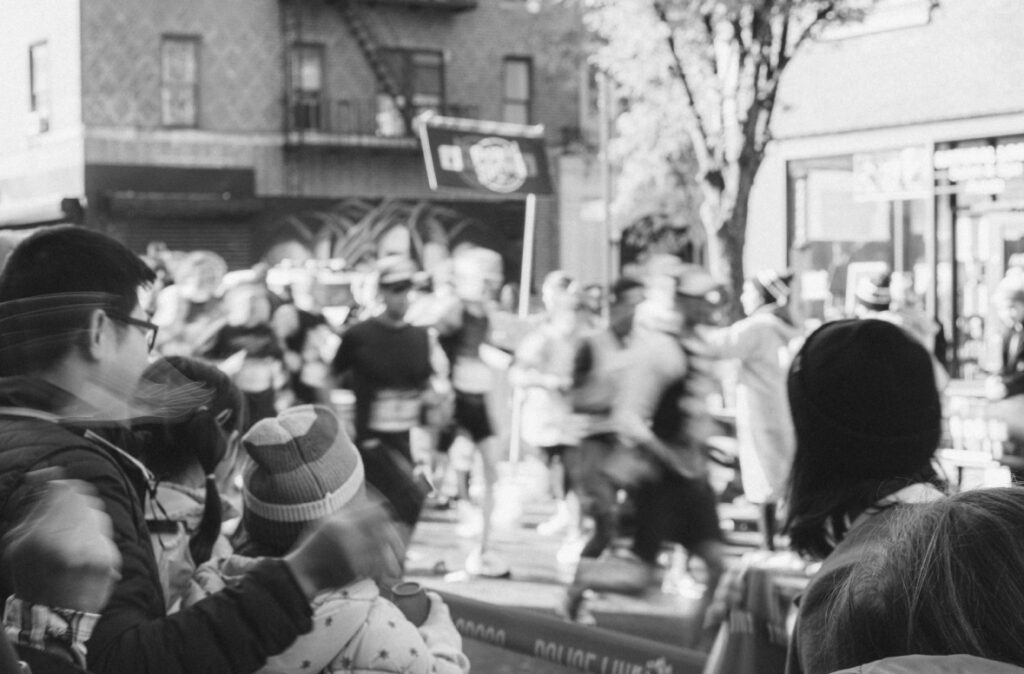 Blurry image of runners streaking past during a marathon while onlookers, in focus, cheer them on.