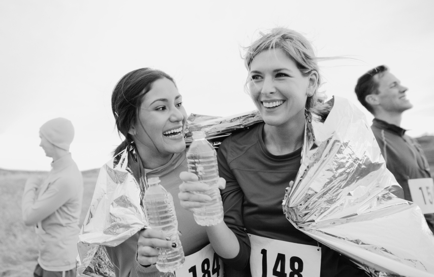 Two female runners celebrate, water bottles in hand, after a race.