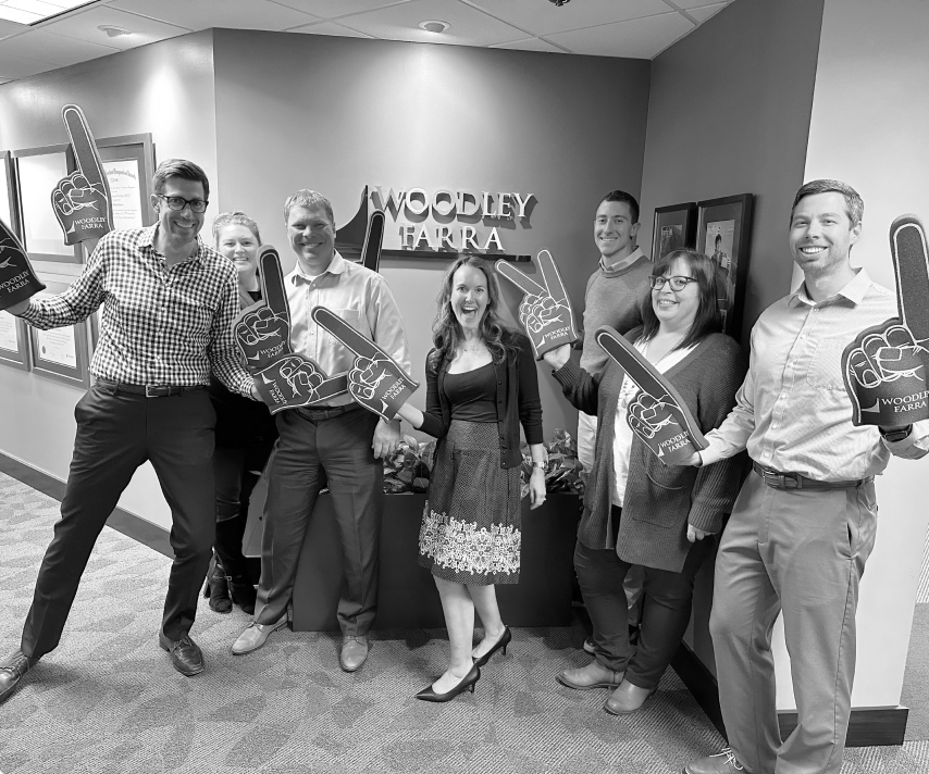 Celebratory photo of some members of the Woodley Farra team holding up the blue foam #1 fingers, celebrating being named the #1 firm in CNBC's 2022 FA 100 rankings.