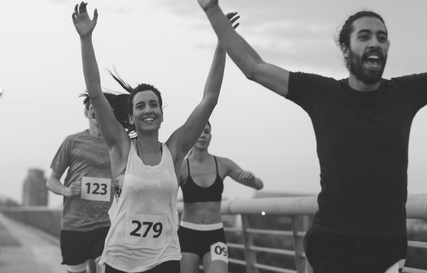 Four runners—two men, two women—raise their arms in celebration as they near the end of the marathon.